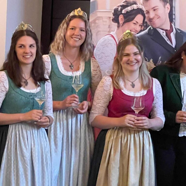 Die drei scheienden Weinhoheiten auf einem Gruppenbild mit Festtracht und einem Glas Wein.